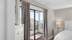 A hotel room with a balcony, a bed, a nightstand with a lamp, and a dresser. - Costa Vista Townhouse #9 (Miramar Beach)