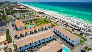 A coastal hotel with multiple buildings, a parking lot, and a beach with umbrellas. - Costa Vista Townhouse #9 (Miramar Beach)