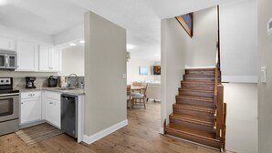 A modern kitchen with white cabinets, a dishwasher, and a wooden staircase leading to a dining area. - Costa Vista Townhouse #9 (Miramar Beach)