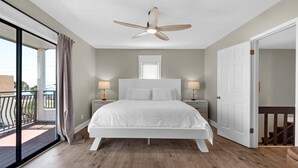 A bedroom with a large bed, two bedside tables with lamps, a ceiling fan, a window with blinds, and a balcony door. - Costa Vista Townhouse #9 (Miramar Beach)