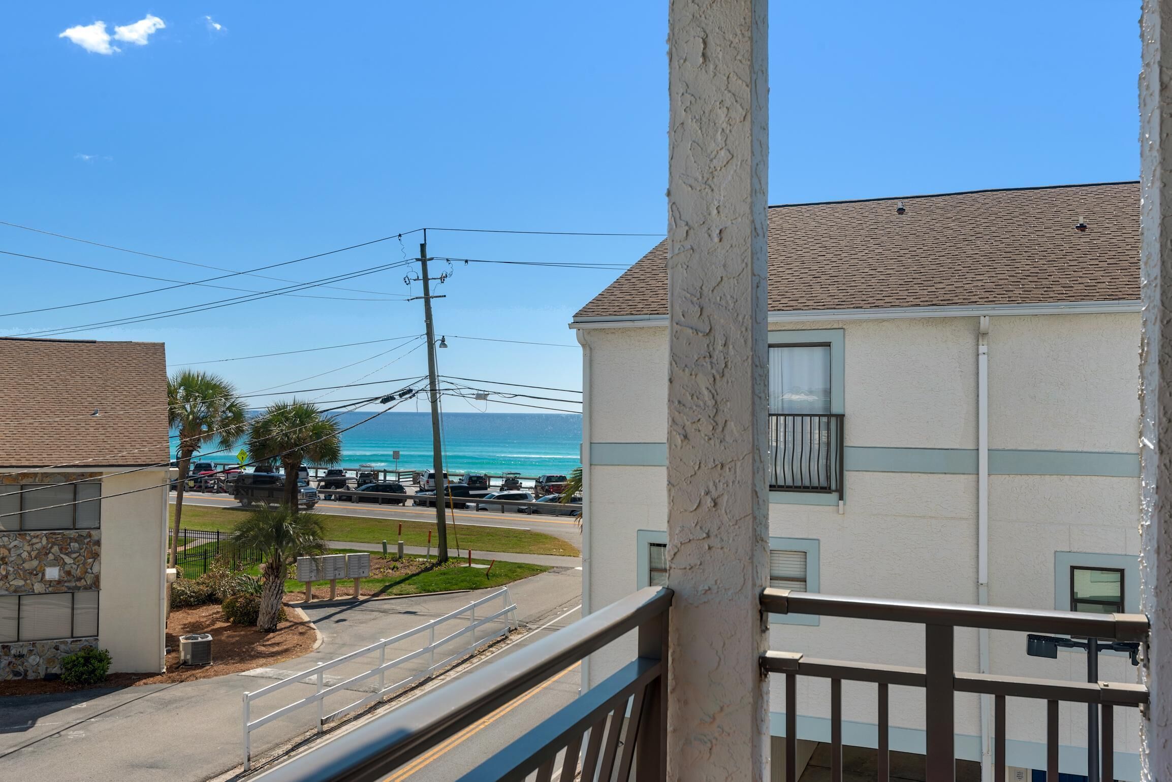 A balcony with a view of the ocean and a parking lot.