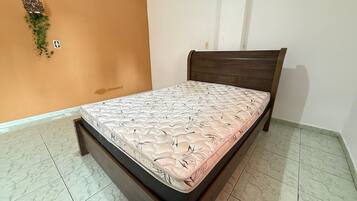 A single bed with a floral mattress in a room with orange walls and tiled flooring.
