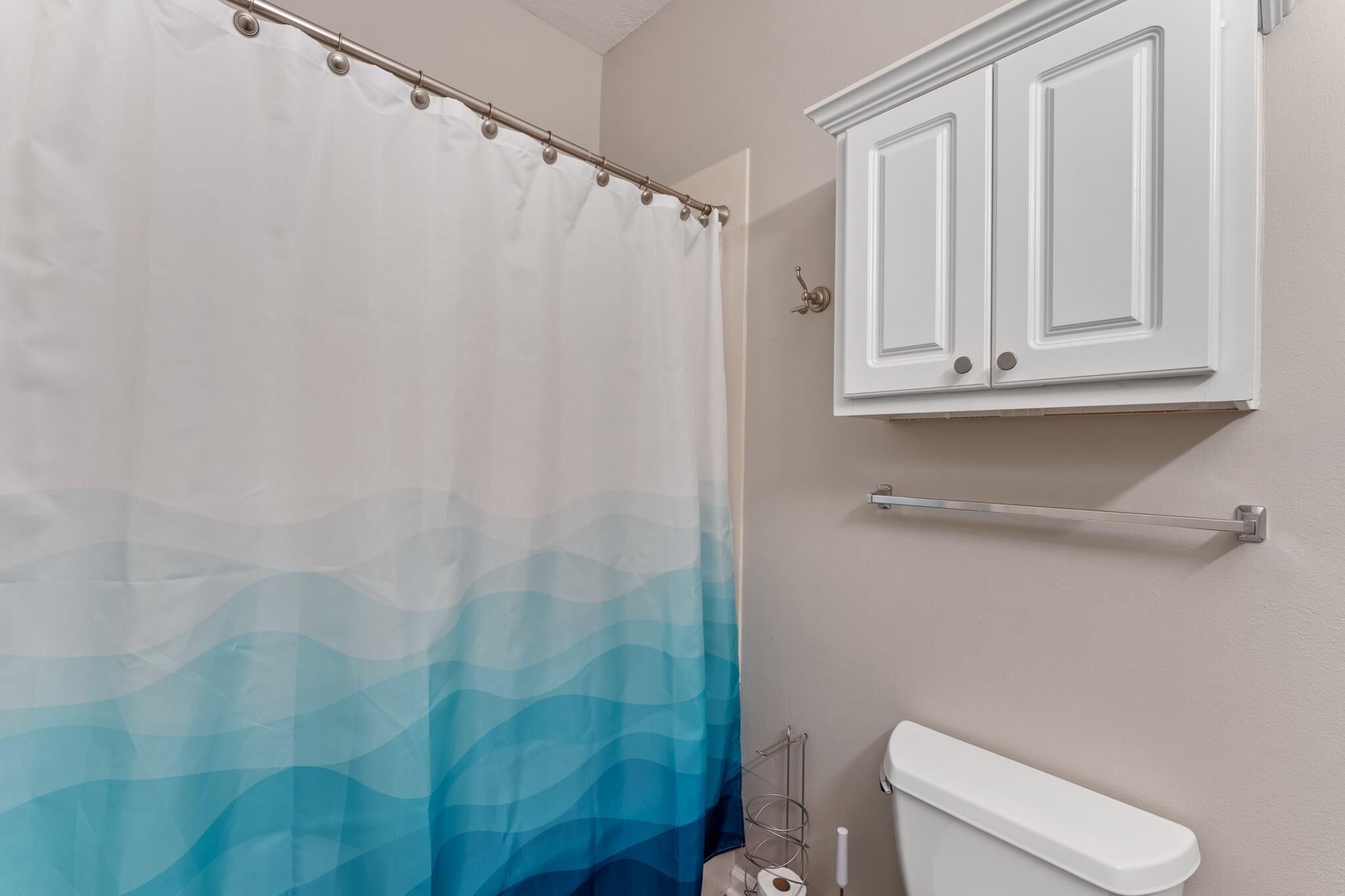 Een badkamer met een wit toilet, een wit kastje erboven en een douchegordijn met blauw verloop.