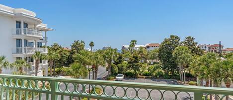 A residential area with a white building featuring balconies, surrounded by palm trees and other greenery.