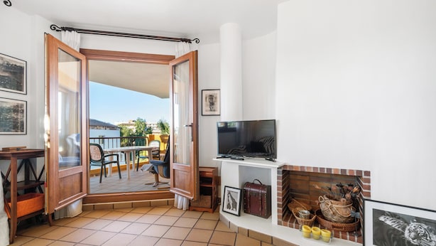 A living room with a TV, fireplace, and outdoor patio visible through an open door. - Punta Prima Beach Apartment Kenya (Punta Prima)