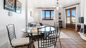 A dining area with a round glass table, black metal chairs, and a chandelier. - Punta Prima Beach Apartment Kenya (Punta Prima)