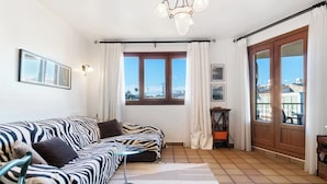 A modern living room with a zebra-patterned sofa, a standing lamp, a large window with curtains, and a view of the cityscape. - Punta Prima Beach Apartment Kenya (Punta Prima)