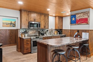 A modern kitchen with wooden cabinets, stainless steel appliances, a granite countertop, and a bar area with stools.