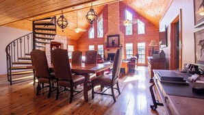 Ein großzügiger Loft-Raum mit hohen Decken, Holzböden, einem Essbereich mit langem Tisch und Stühlen, einem Kamin und großen Fenstern für viel Tageslicht.