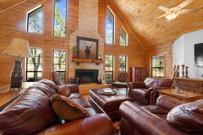 A spacious living room with leather sofas, a fireplace, and large windows.