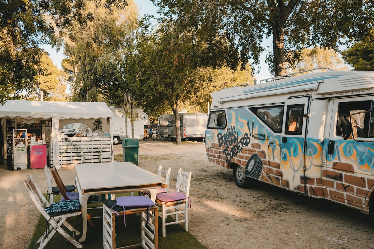 Ein Campingplatz mit Essbereich, einem weißen Tisch und Stühlen, sowie ein Wohnmobil mit Graffiti.