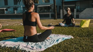 A person sitting on a blanket in a grassy area with buildings in the background. - Lloret de Mar Camping (Lloret de Mar)