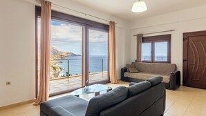 Ein modernes Wohnzimmer mit einer Couch, einem Glastisch und Blick auf das Meer.