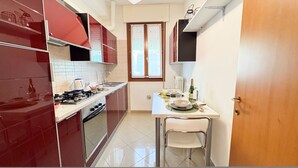 Una cucina compatta con mobili rossi, un fornello a gas, un lavello e una zona pranzo con una sedia e un tavolo.