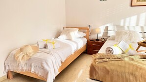 A neatly made bed with white linens and a beige throw blanket, a wooden nightstand with a lamp and an alarm clock, and a fluffy white pillow on the adjacent bed. - Casa Dora in Chioggia (Chioggia)