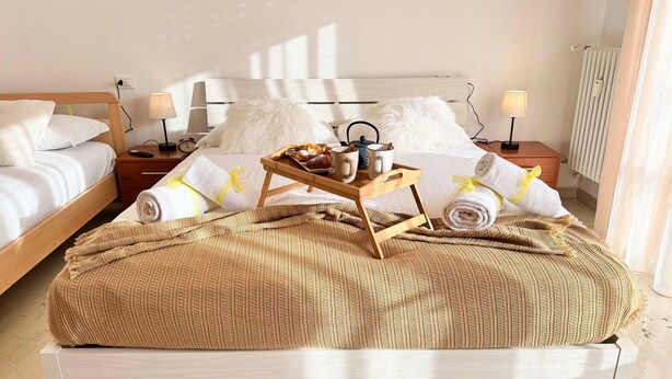 Un letto rifatto con cura, un vassoio con prodotti per la colazione, asciugamani e una coperta su una piattaforma in legno.