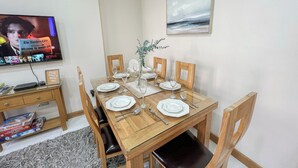 A dining area with a wooden table set for four, a television displaying a show, and a motivational quote sign. - Cosy 4-Bed, 2-Bath flat with AC near Hyde Park , Paddington , Marylebone (London)
