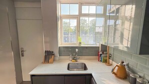 A modern kitchen with a built-in dishwasher, a sink, and a window with a view of trees. - Cosy 4-Bed, 2-Bath flat with AC near Hyde Park , Paddington , Marylebone (London)