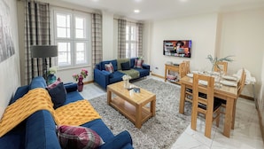 A living room with a sofa set, a coffee table, a dining table with chairs, and a TV mounted on the wall. - Cosy 4-Bed, 2-Bath flat with AC near Hyde Park , Paddington , Marylebone (London)