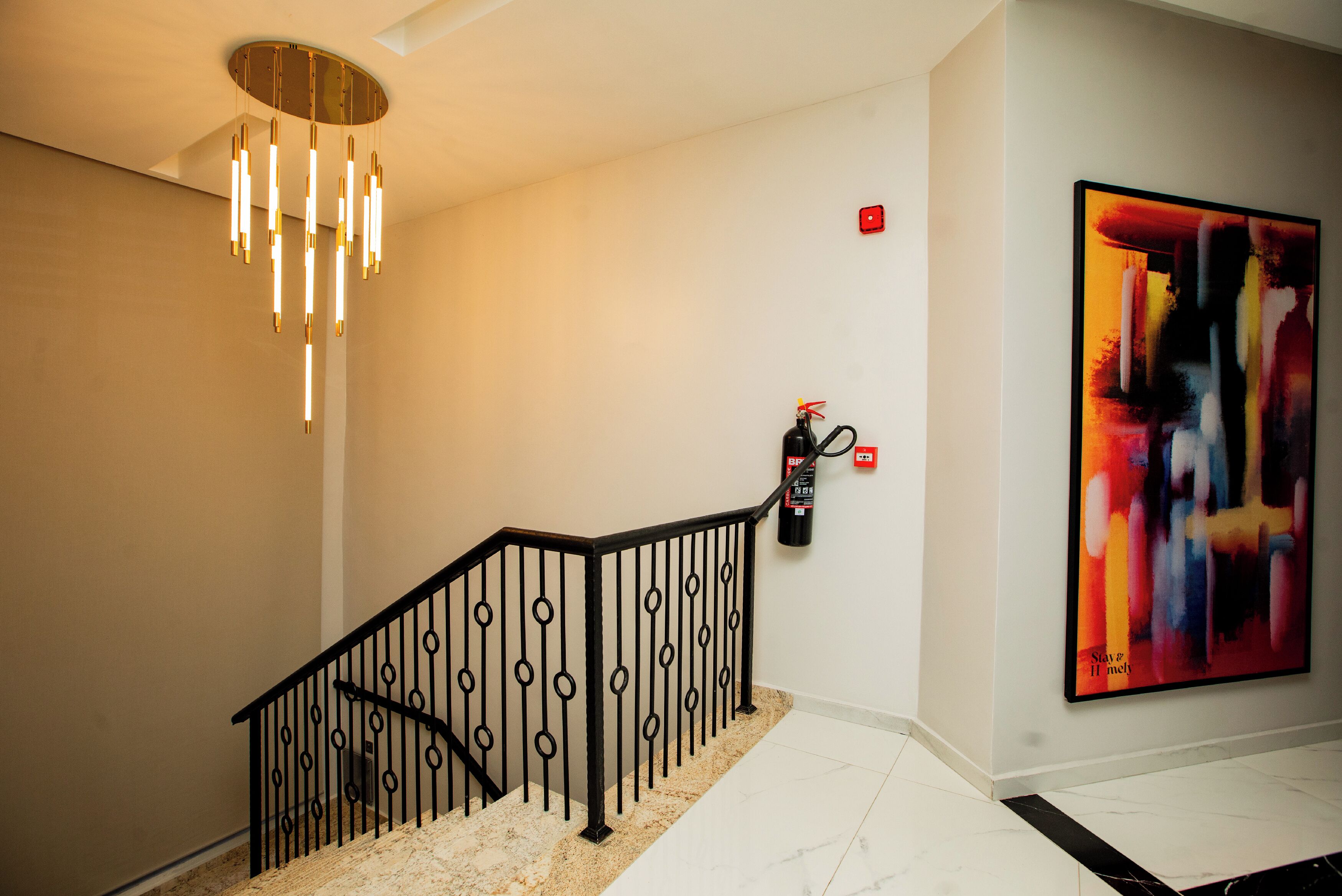 Un intérieur moderne avec un escalier, un lustre, un extincteur et un grand tableau abstrait.