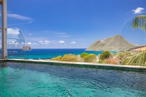 A clear view of a swimming pool with a mountain and ocean in the background.