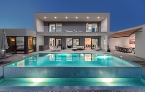 Een modern huis met twee verdiepingen, een groot zwembad, terrasmeubilair en een eethoek.