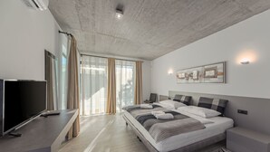 A modern bedroom with a large bed, bedside tables, a flat-screen TV, and a window with curtains.