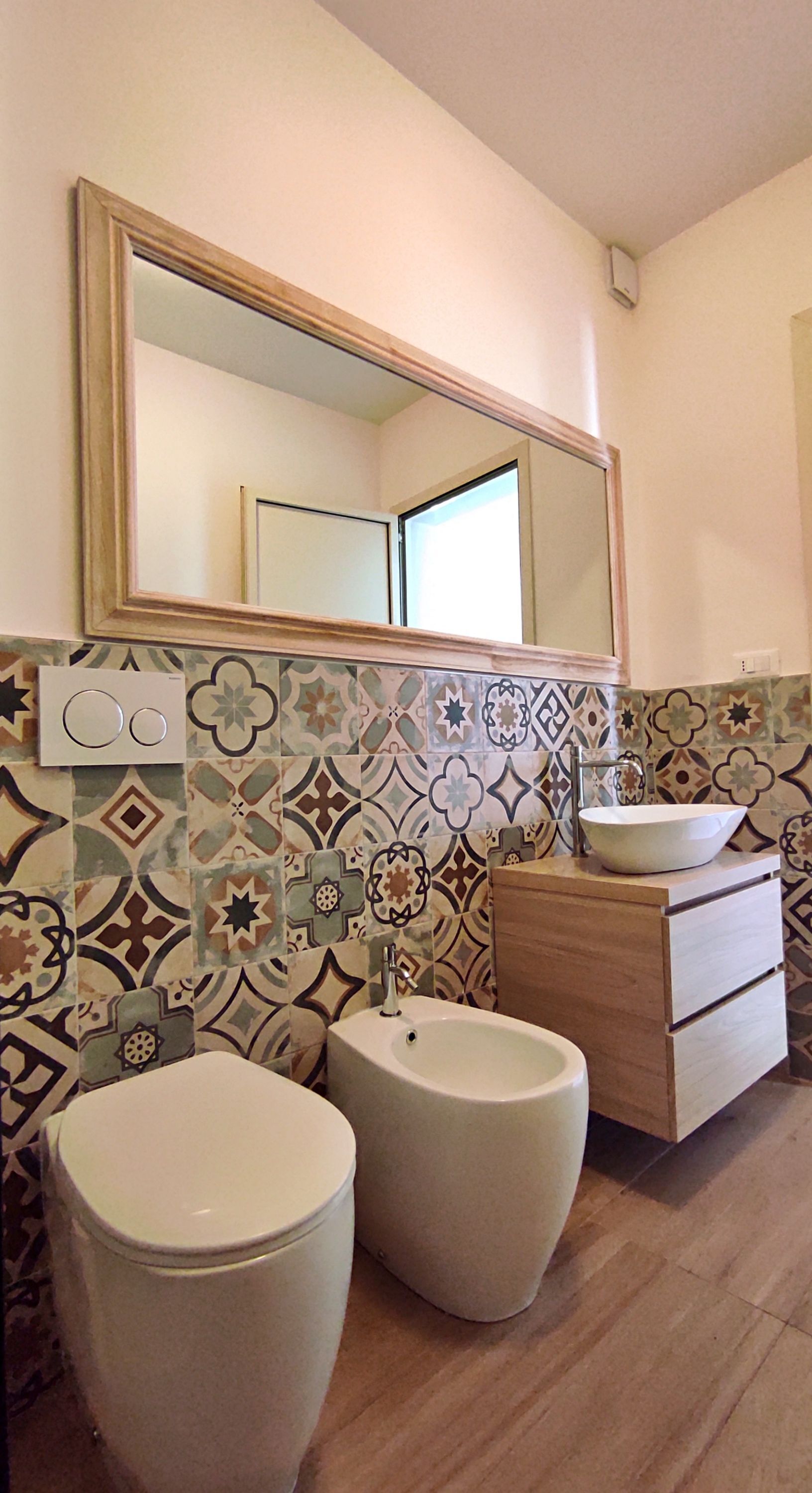 A bathroom with two toilets, a bidet, a sink, a mirror, and a wooden cabinet.