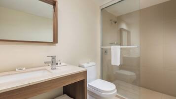 A modern bathroom with a sink, mirror, toilet, and glass-enclosed shower.
