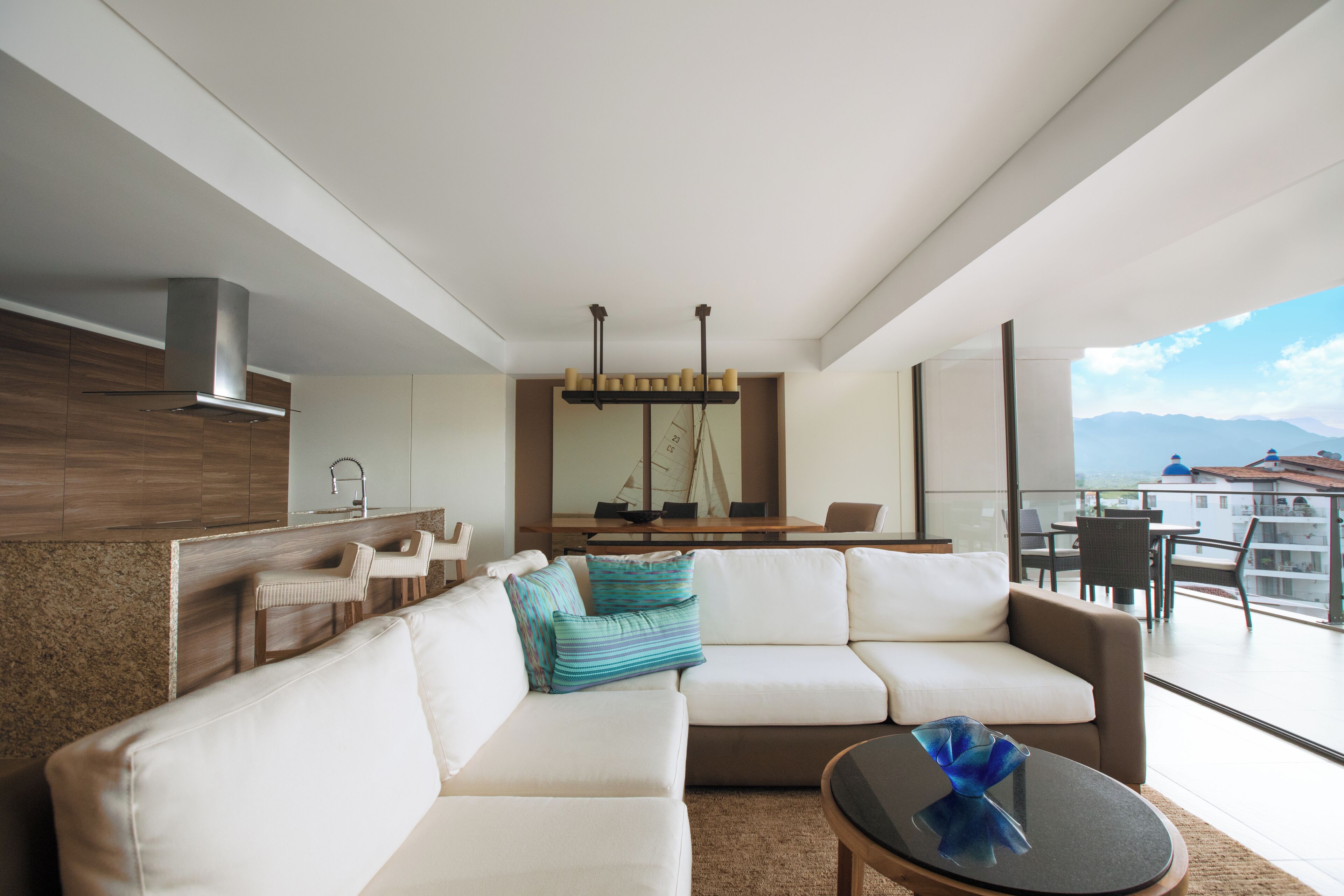A modern living room with a sofa, chairs, a coffee table, and a dining area with a view of the mountains.