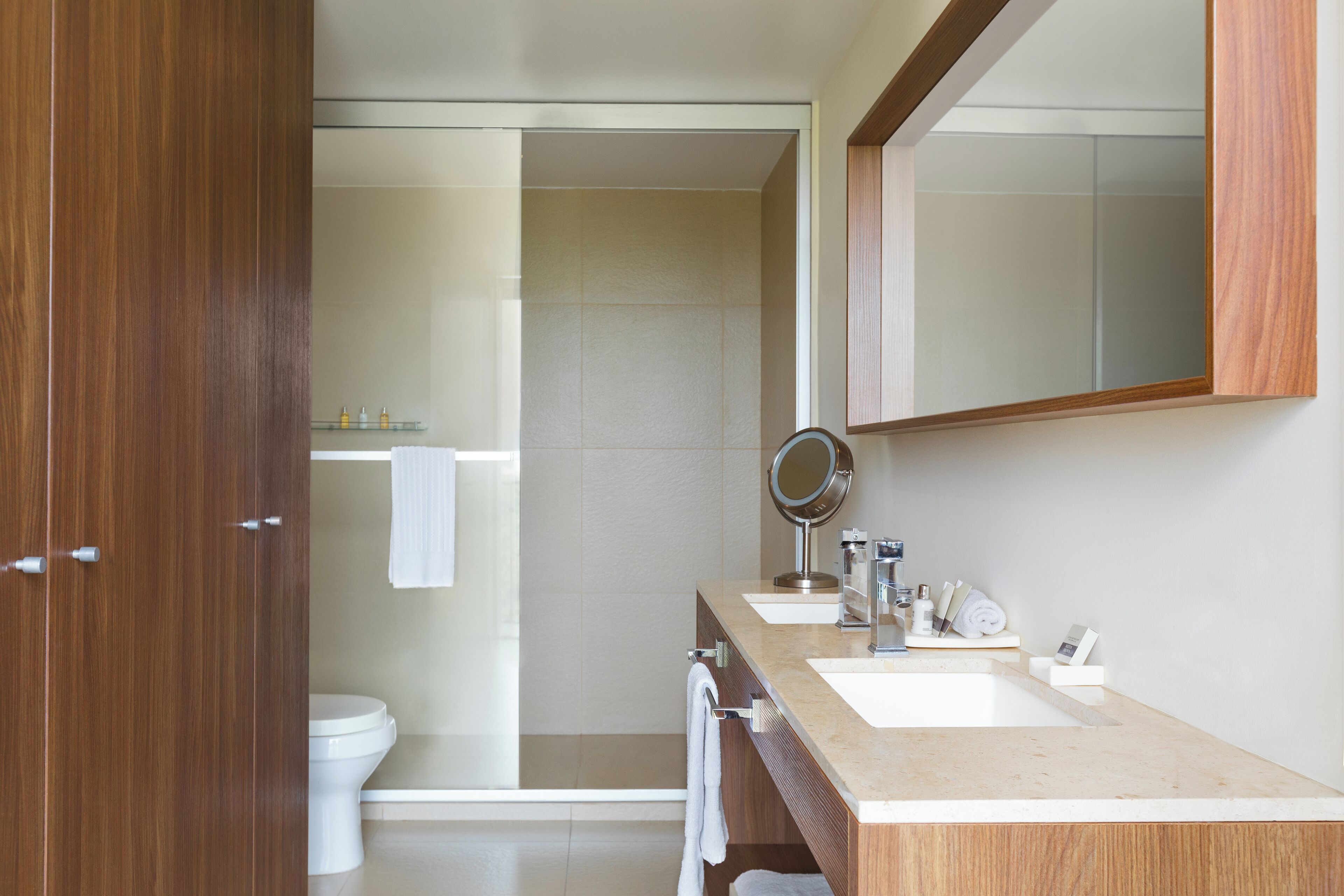 Un baño moderno con tocador de madera, dos lavamanos, un espejo y un inodoro.