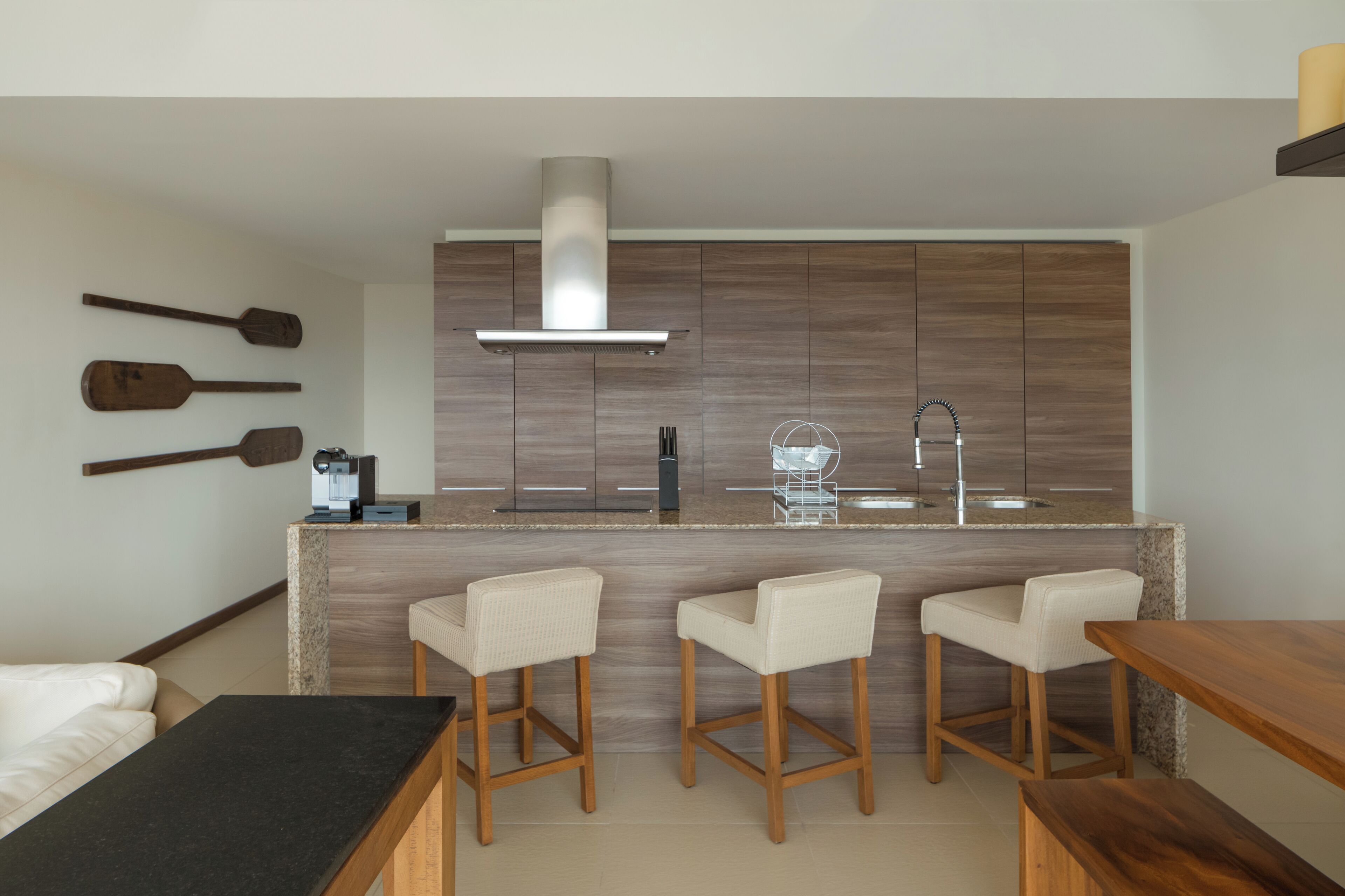 A modern kitchen with wooden cabinets, a stainless steel range hood, and a bar area with three bar stools.