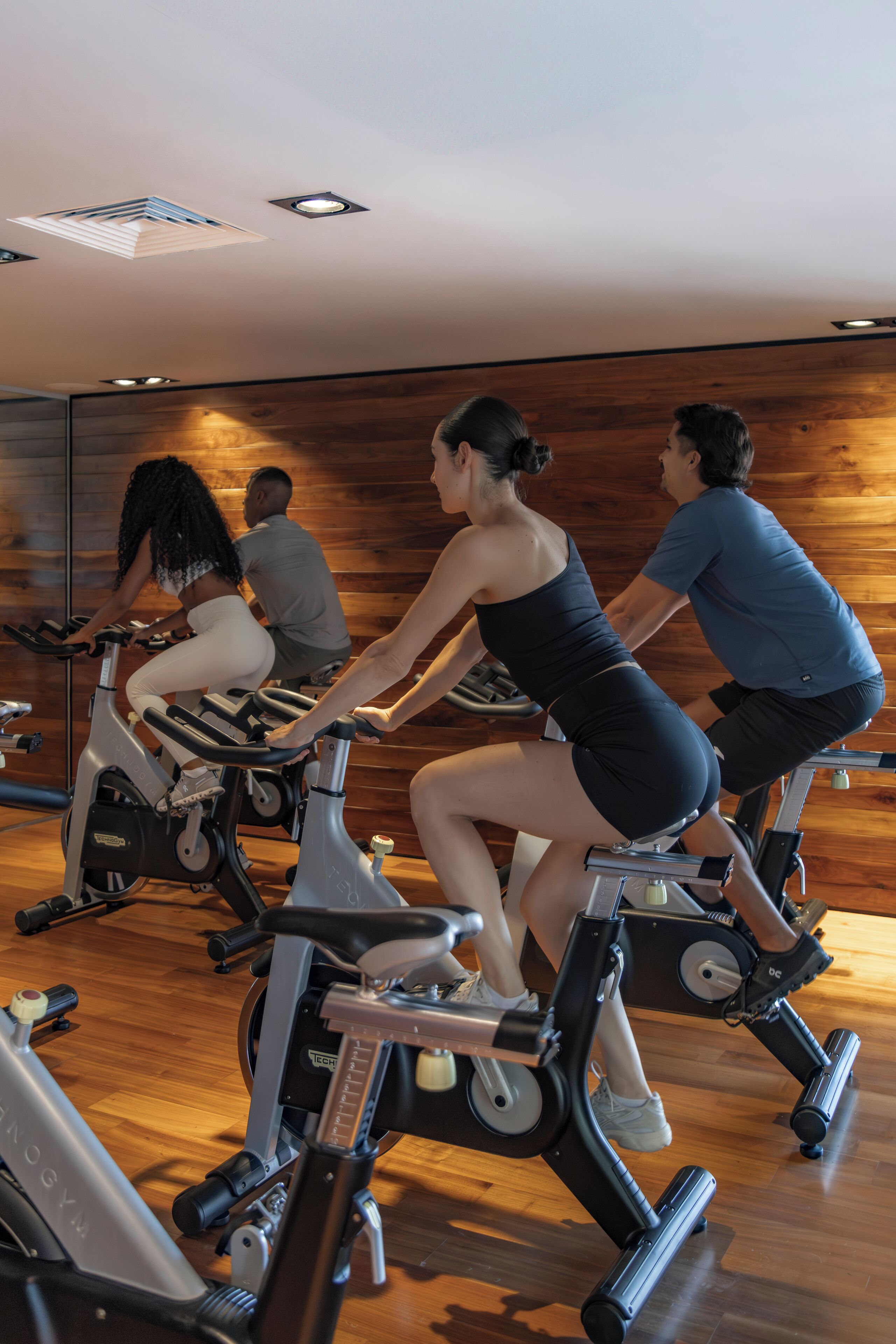 A gym with stationary bikes, wooden walls, and a mirrored ceiling.