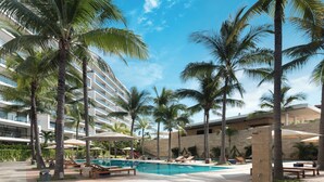 A pool area with palm trees, lounge chairs, and a modern building with balconies. - Live Aqua Private Residences Vallarta (Puerto Vallarta)