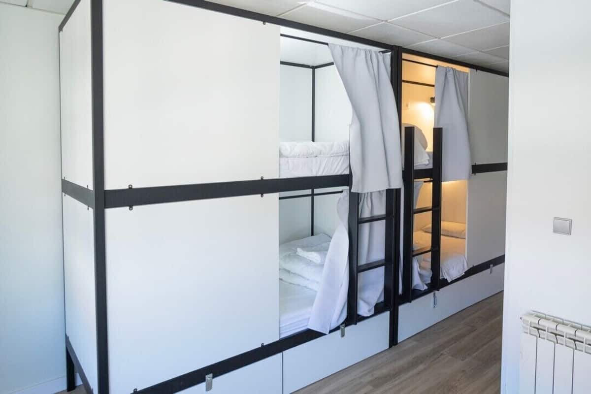 Une chambre de dortoir avec des lits superposés, une fenêtre avec des rideaux et un radiateur au mur.