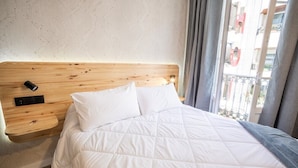 A neatly made bed with a wooden headboard, a bedside table with a phone, and a view of the outside balcony. - HOTEL NAUTICO (Vigo)