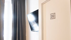 A room with a door labeled '202', a window with curtains, and a mounted television. - HOTEL NAUTICO (Vigo)