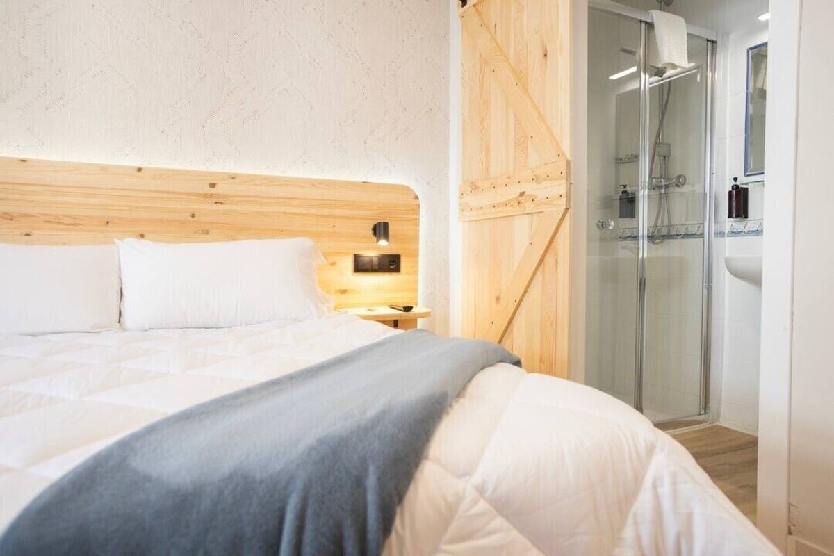 Une chambre à coucher avec une tête de lit en bois, un lit avec une literie blanche, une table de chevet avec une lampe et une cabine de douche en verre.