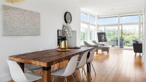 A dining area with a wooden table, white chairs, a large menu on the wall, and a view of the outdoors through large windows. - Bauhinia House: Spa Access and Lakeside Home, Lower Mill Estate (Somerford Keynes)