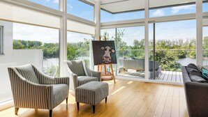 A spacious room with large windows, a painting on easel, and a view of greenery. - Bauhinia House: Spa Access and Lakeside Home, Lower Mill Estate (Somerford Keynes)