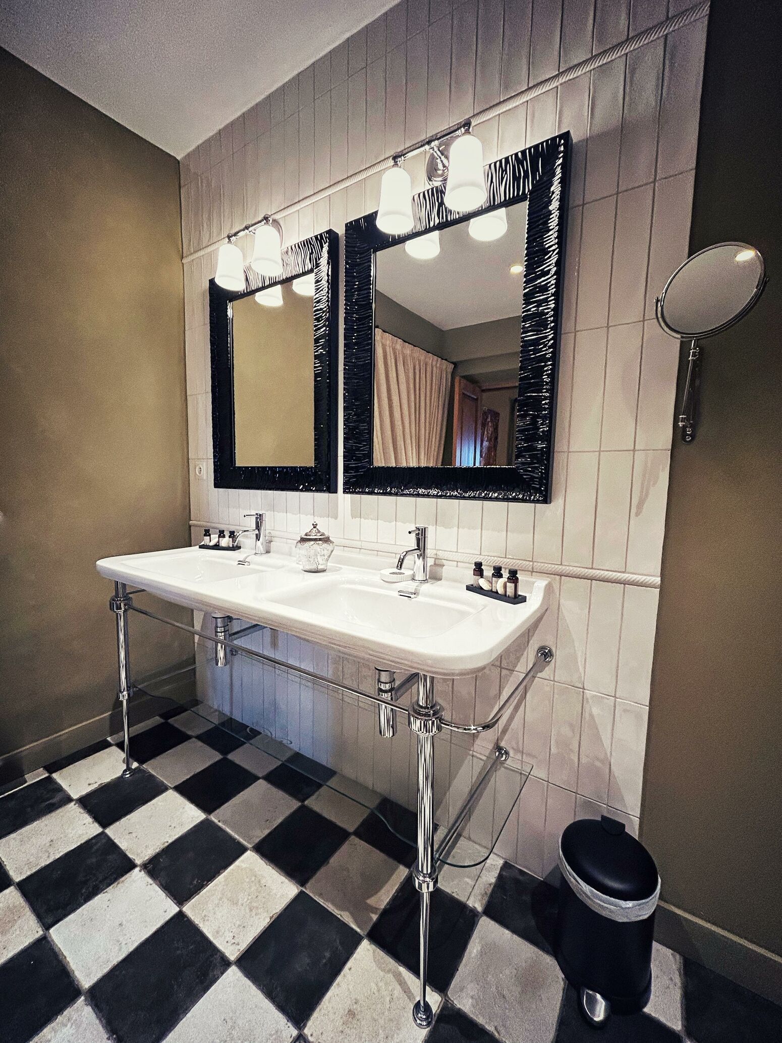 A bathroom with a white sink, two mirrors, and a black trash bin.