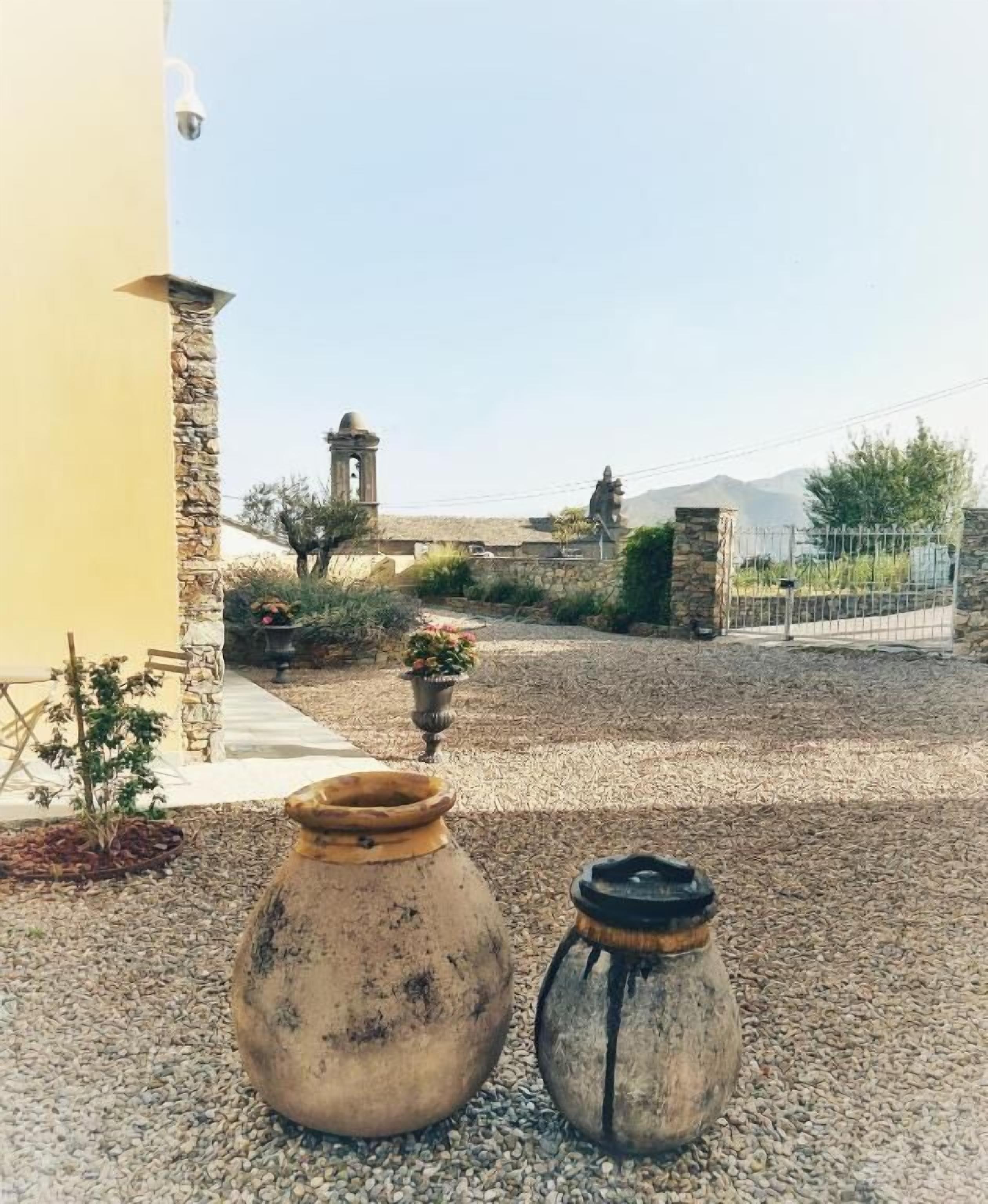 Two large ceramic pots on a gravel surface, a stone wall, and a building with a tower in the background.