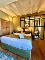 Habitación de hotel con una cama grande, un armario de madera y un espejo que refleja el baño.