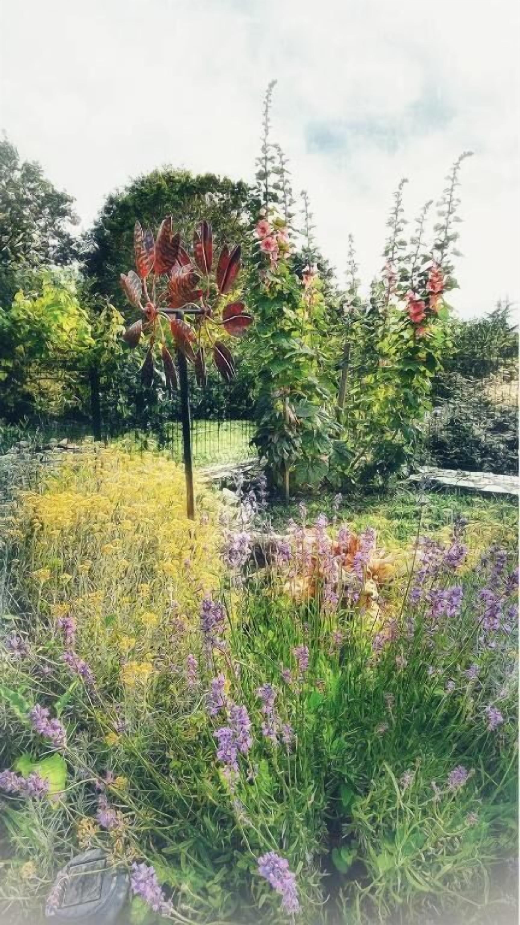 A garden with various plants and flowers, including purple and yellow blooms, and a tree with red leaves.