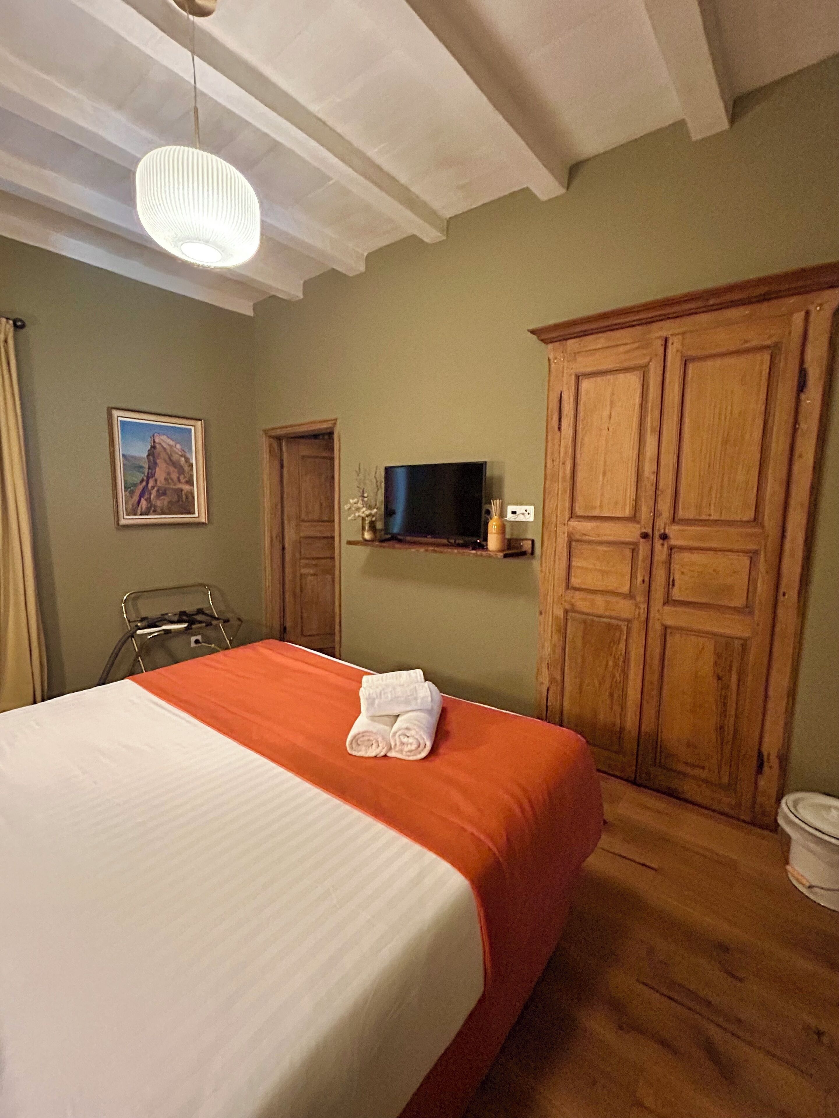 Habitación de hotel con una cama, televisión, armario de madera y un cuadro en la pared.