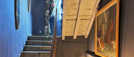 A staircase with a wooden railing, a painting on the wall, and a series of illuminated globes on a wooden table.