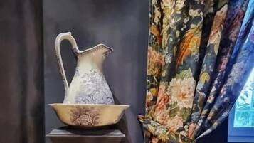 Una mesa oscura con una jarrón y un cuenco encima, junto a una ventana con cortinas florales.