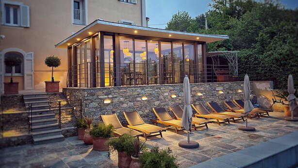 A modern villa with a glass-enclosed patio, stone steps, and outdoor seating with umbrellas. - À Villa di Rutali (Rutali)