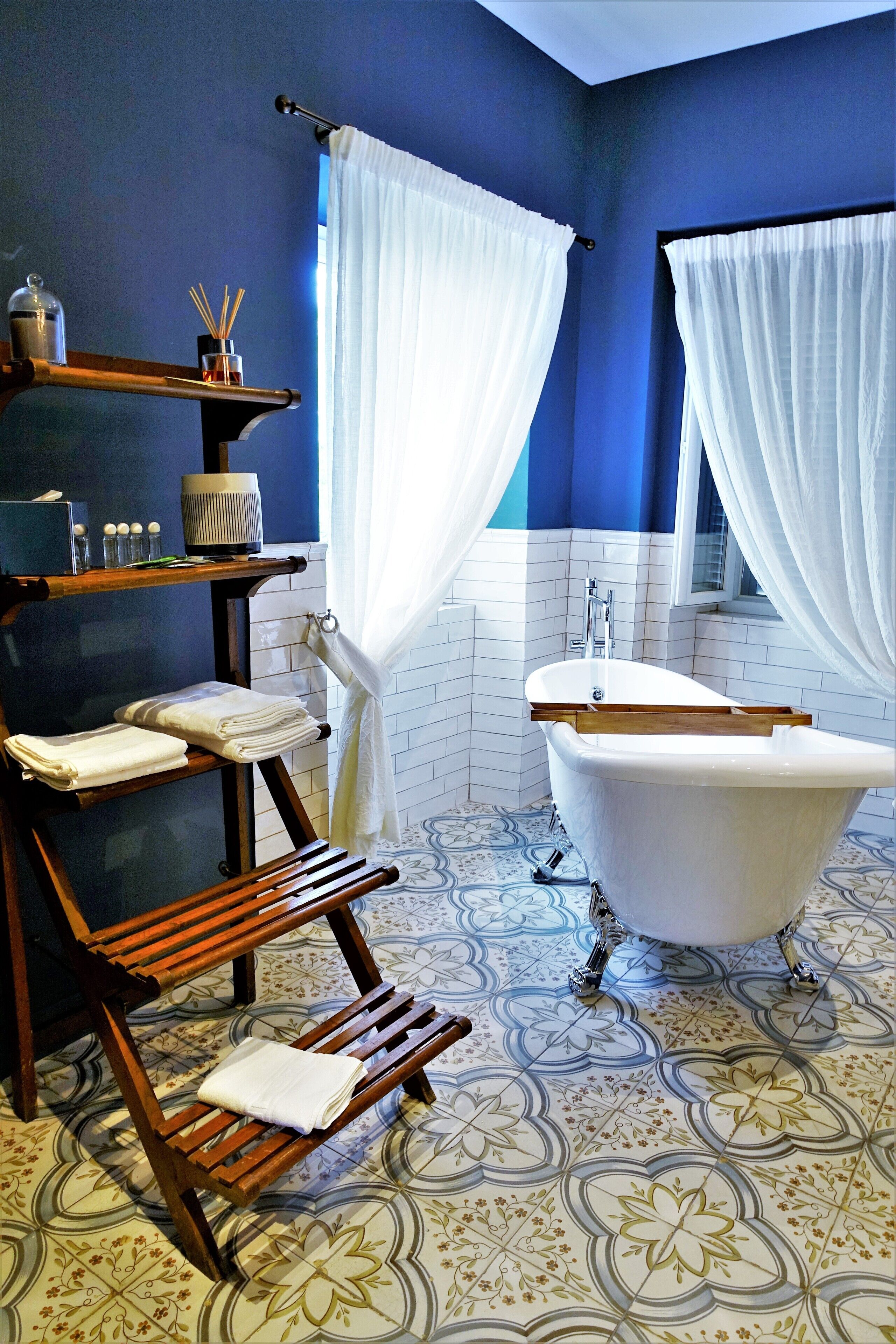 A bathroom with a bathtub, a wooden bench, a shelf with toiletries, and a patterned floor.