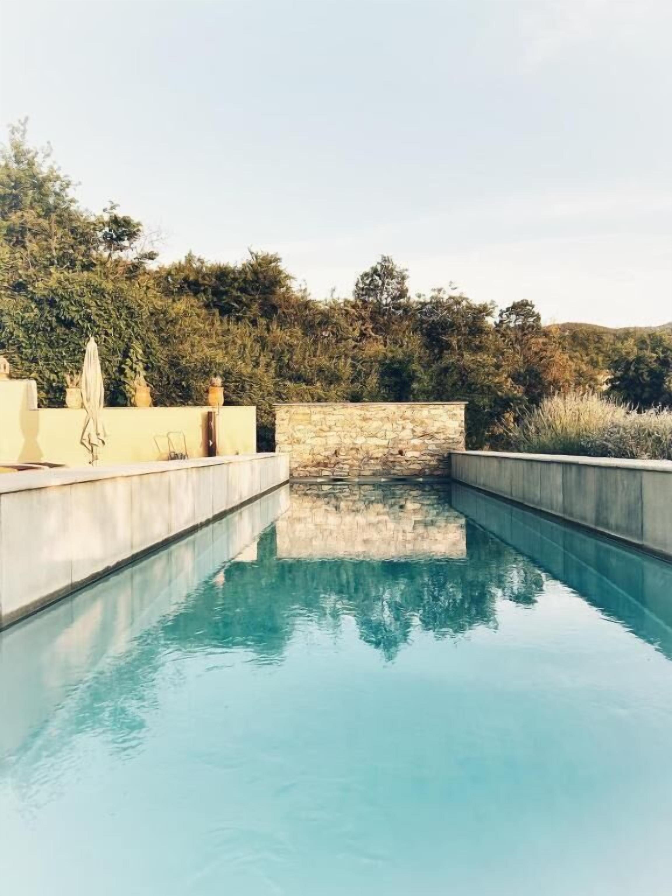 A swimming pool with a stone wall and a view of trees.